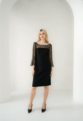 Woman wearing a black dress with sheer sleeves against a white background